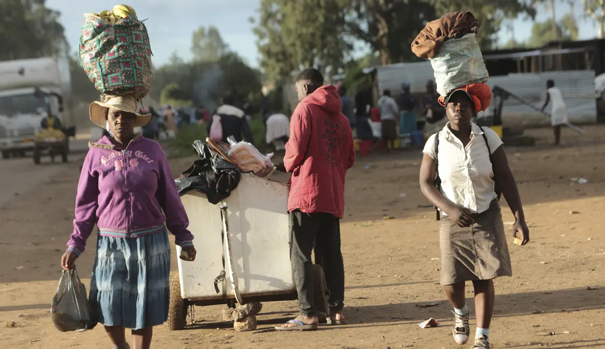 Dua perempuan membawa berbagai barang di kepala mereka saat mereka berjalan di pinggiran kota padat Mbare di Harare, Zimbabwe, Rabu, (26/2/2020). Emmerson Mnangagwa adalah presiden Zimbabwe saat ini. (AP Photo/Tsvangirayi Mukwazhi)