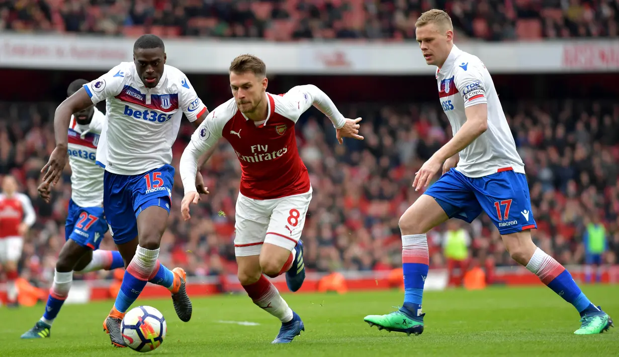 Gelandang Arsenal, Aaron Ramsey, melewati kepungan pemain Stoke pada laga Premier league di Stadion Emirates, London, Minggu (1/4/2018). Arsenal menang 3-0 atas Stoke. (AFP/Oliver Greenwood)