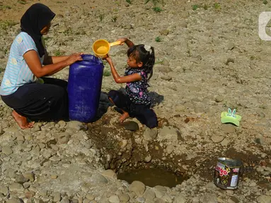 Seorang anak bersama ibunya mengambil air pada galian sumur di tengah aliran Sungai Cihoe, Kamis (28/9/2023). Warga Desa Sukagalih, Jonggol, Bogor, mengalami kesulitan air bersih di tengah fenomena El Nino yang menyebabkan musim kemarau berkepanjangan. (merdeka.com/Arie Basuki)