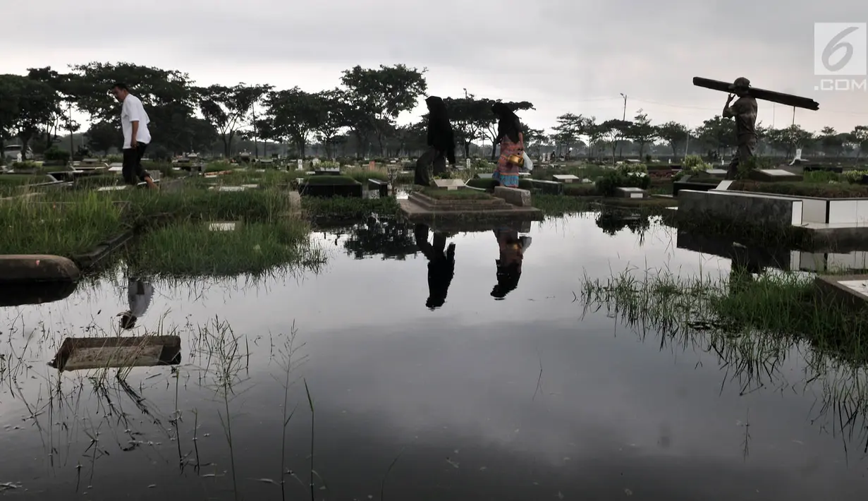Peziarah melintasi makam yang terendam banjir di Taman Pemakaman Umum (TPU) Semper, Jakarta, Selasa (4/12). (Merdeka.com/Iqbal S. Nugroho)