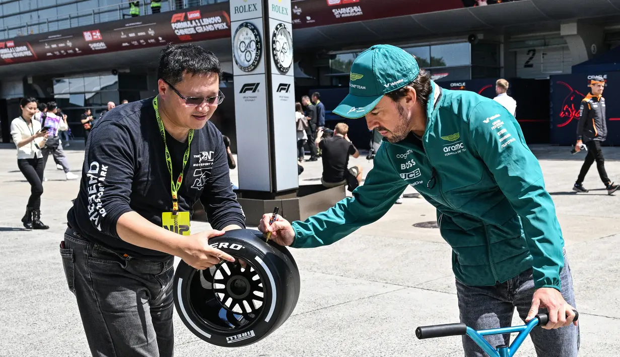 Pembalap Aston Martin asal Spanyol, Fernando Alonso (kanan) memberikan tanda tangan kepada seorang penggemar di paddock di sirkuit Shanghai International pada 18 April 2024. (Hector RETAMAL/AFP)