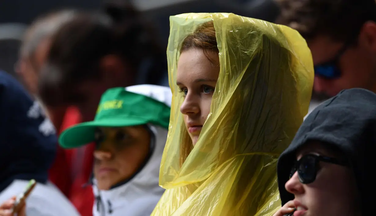 Seorang wanita memakai jas hujan menyaksikan pertandingan tunggal tunggal pria antara petenis Italia Andreas Seppi dan petenis Prancis Corentin Moutet pada hari pertama turnamen tenis Australia Terbuka di Melbourne (15/1). (AFP Photo/Saeed Khan)