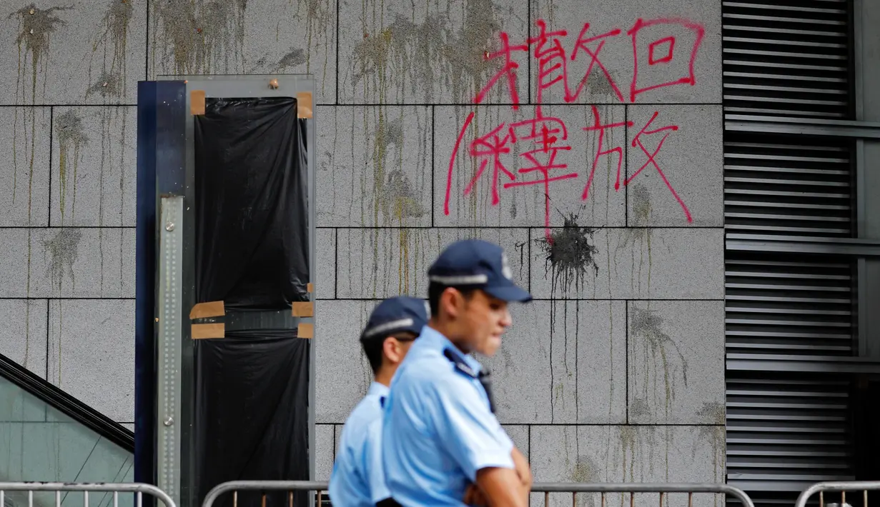 Polisi berjaga-jaga di depan tembok bertulis kata-kata China 'Penarikan dan Pembebasan' di pintu masuk utama kantor polisi di Hong Kong, Sabtu (22/6/2019). Markas polisi tersebut jadi korban aksi vandalime demonstran dalam lanjutan aksi unjuk rasa menolak RUU Ekstradisi. (AP Photo/Vincent Yu)