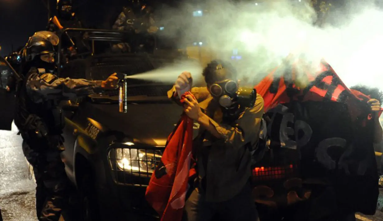 Polisi anti huru hara terlihat menyemprotkan gas air mata ke salah satu pengunjuk rasa di sekitar Stadion Maracana, Rio de Janeiro, Brasil, (15/6/2014). (AFP PHOTO/Tasso Marcelo)