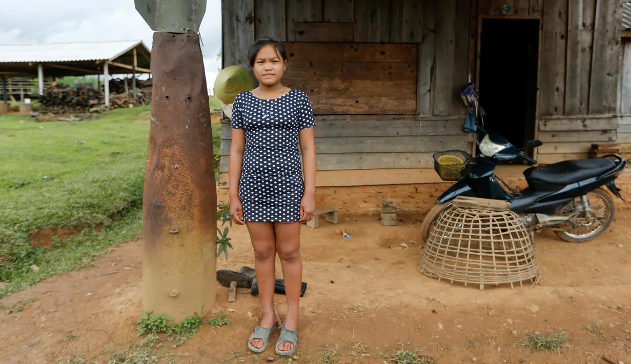 Seorang gadis berpose di samping bom yang dijatuhkan oleh pesawat AS di pintu masuk rumahnya di Desa Ban Napia, Provinsi Xieng Khouang, Laos (03/9). Sekitar 30 persen bom yang dijatuhkan gagal meledak, termasuk bom klaster.(REUTERS/Jorge Silva)
