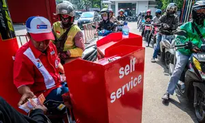 Seorang pekerja SPBU (kiri) menerima pembayaran dari pengendara yang mengantre untuk mengisi bahan bakar sepeda motor mereka di sebuah Stasiun Pengisian Bahan Bakar Umum (SPBU), Jakarta pada Rabu 1 April 2026. Pemerintah resmi tidak mengubah harga Bahan Bakar Minyak (BBM) di dalam negeri, baik harga BBM subsidi maupun non subsidi. (BAY ISMOYO/AFP)