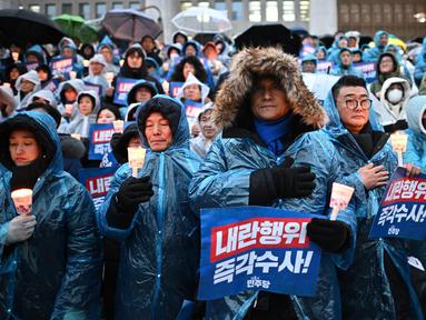 Para pengunjuk rasa mengenakan ponco di tengah hujan saat mereka mengambil bagian dalam aksi menyalakan lilin yang menyerukan penggulingan Presiden Korea Selatan Yoon Suk Yeol di tangga Majelis Nasional di Seoul pada Kamis 5 Desember 2024. (Philip FONG/AFP)