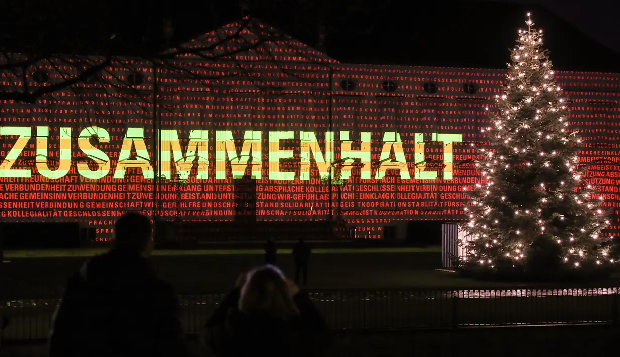 Pengunjung menikmati pemandangan Istana Bellevue yang diterangi proyeksi cahaya bertuliskan "Zusammenhalt", yang bermakna saling bergandengan tangan, di Berlin, 17 Desember 2020. Pertunjukan cahaya bertema "Lichtblick" ini untuk menyerukan solidaritas demi melawan pandemi COVID-19 (Xinhua/Shan Yuqi)