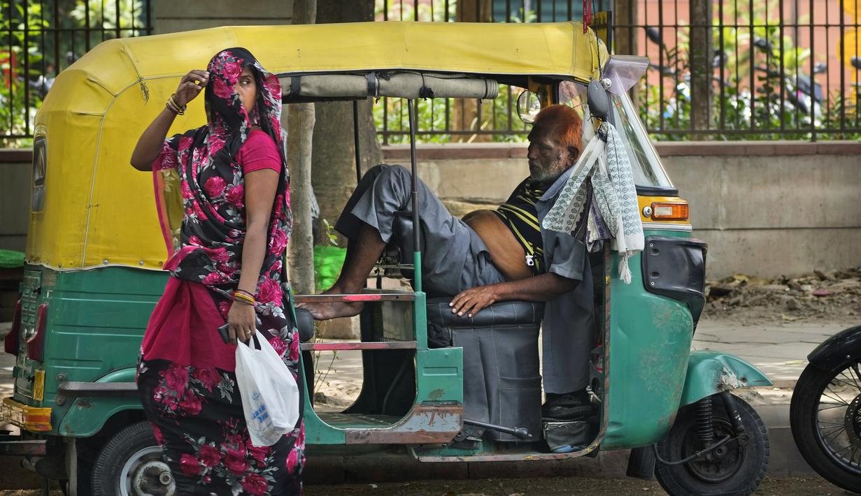<p>Seorang pengemudi bajaj yang kelelahan karena panas yang hebat beristirahat di dalam kendaraannya ketika seorang perempuan yang menutupi wajah berjalan melewatinya, di New Delhi, India, Kamis (19/5/2022). Meskipun hujan sporadis, ibu kota India itu masih menghadapi kondisi panas yang ekstrem. (AP Photo/Manish Swarup)</p>
