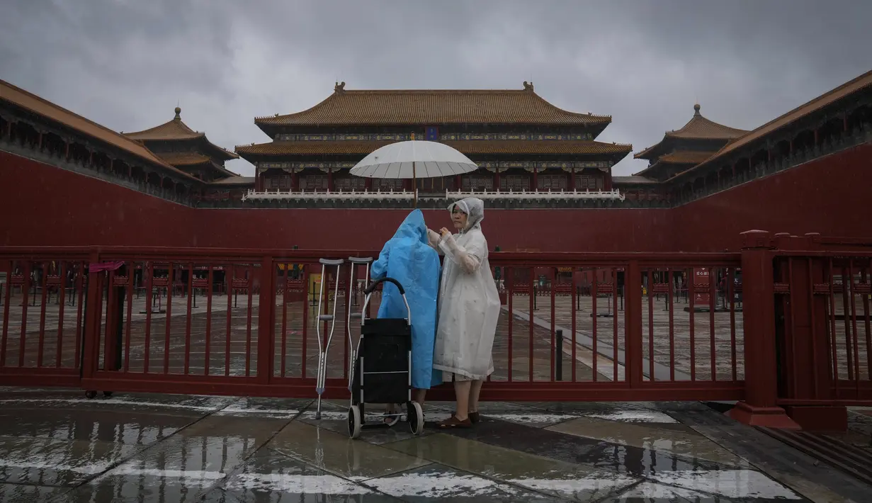 Pengunjung yang ditutupi jas hujan dan payung berdiri di gerbang masuk Kota Terlarang yang tertutup saat hujan badai membasahi Beijing, China, Minggu (30/7/2023). (AP Photo/Andy Wong)
