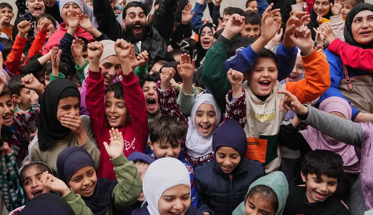 Hadirnya para relawan tersebut untuk memberikan hiburan dan dukungan psikologis bagi anak-anak di Lebanon, terutama di tengah situasi sulit. Tampak dalam foto, anak-anak bersorak gembira saat para sukarelawan menyiapkan bingkisan makanan dan manisan Idulfitri untuk keluarga-keluarga pengungsi yang tinggal di sebuah universitas negeri yang diubah menjadi tempat penampungan setelah serangan udara Israel di Beirut, Lebanon, Jumat, 20 Maret 2026. (AP Photo/Hassan Ammar)