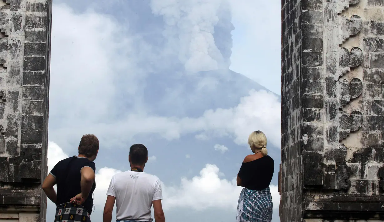 Wisatawan melihat asap Gunung Agung di sebuah kuil di Kabupaten Karangasem, Bali, (27/11). Pihak berwenang telah mengantisipasi dampak yang ditimbulkan oleh aktivitas Gunung Agung dengan menutup Bandara Ngurah Rai. (AP Photo / Firdia Lisnawati)