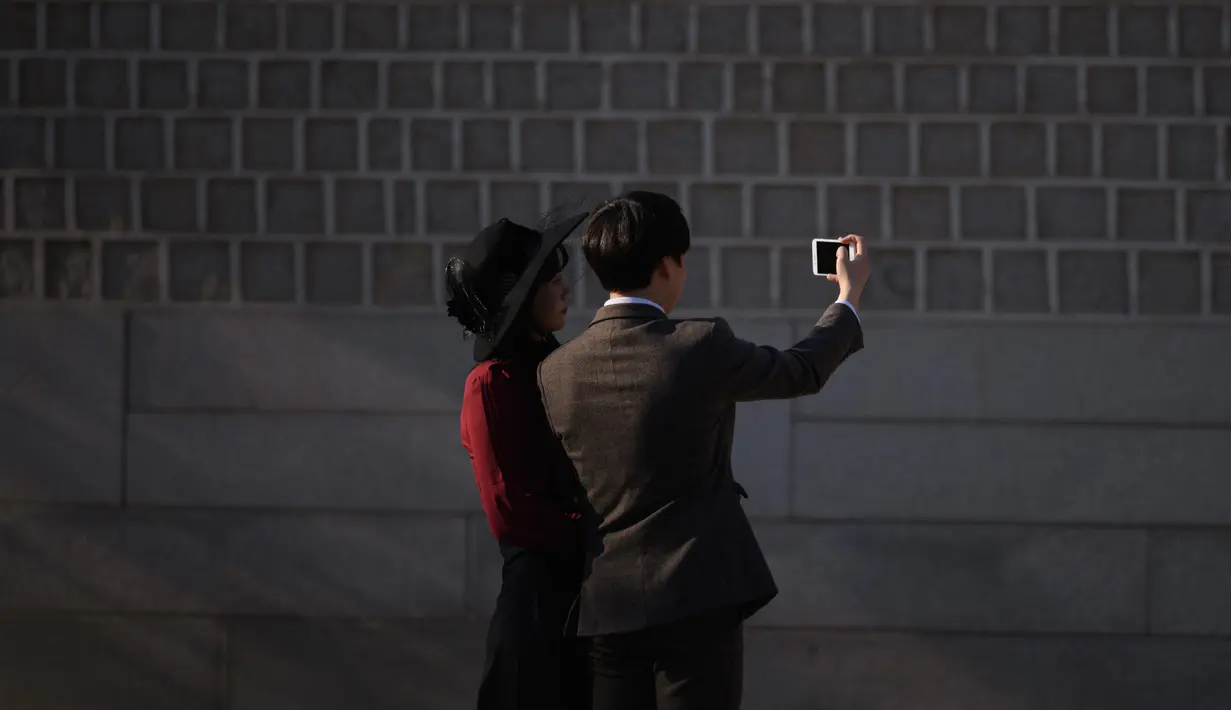 Pasangan menggunakan ponsel berselfie di istana Changdeokgung di Seoul , Korea Selatan (2/4). Korea Selatan sedang bersiap untuk meluncurkan jaringan seluler 5G pertama di dunia pada 5 April. (AFP Photo/Ed Jones)