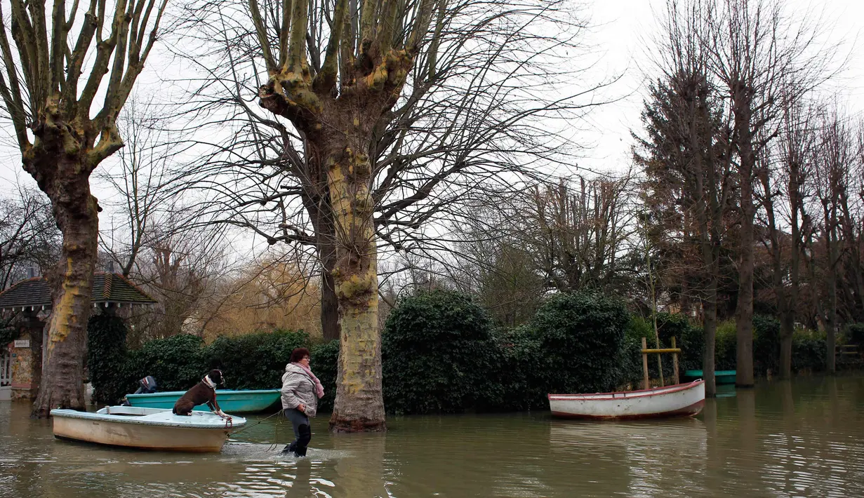 Seorang wanita menggunakan perahu membawa seekor anjing saat berusaha menuju rumahnya di sungai Seine, di Villennes sur Seine, sebelah barat Paris (30/1). (AP Photo / Thibault Camus)
