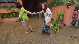 Warga berjalan di jalanan berlumpur setelah banjir akibat hujan deras yang dibawa Topan Kalmaegi di sebuah permukiman di Kota Cebu, Filipina tengah, pada Selasa 4 November 2025. Sedikitnya dua orang tewas, serta ribuan warga lainnya mengungsi ke tempat yang lebih aman. (Alan TANGCAWAN/AFP)