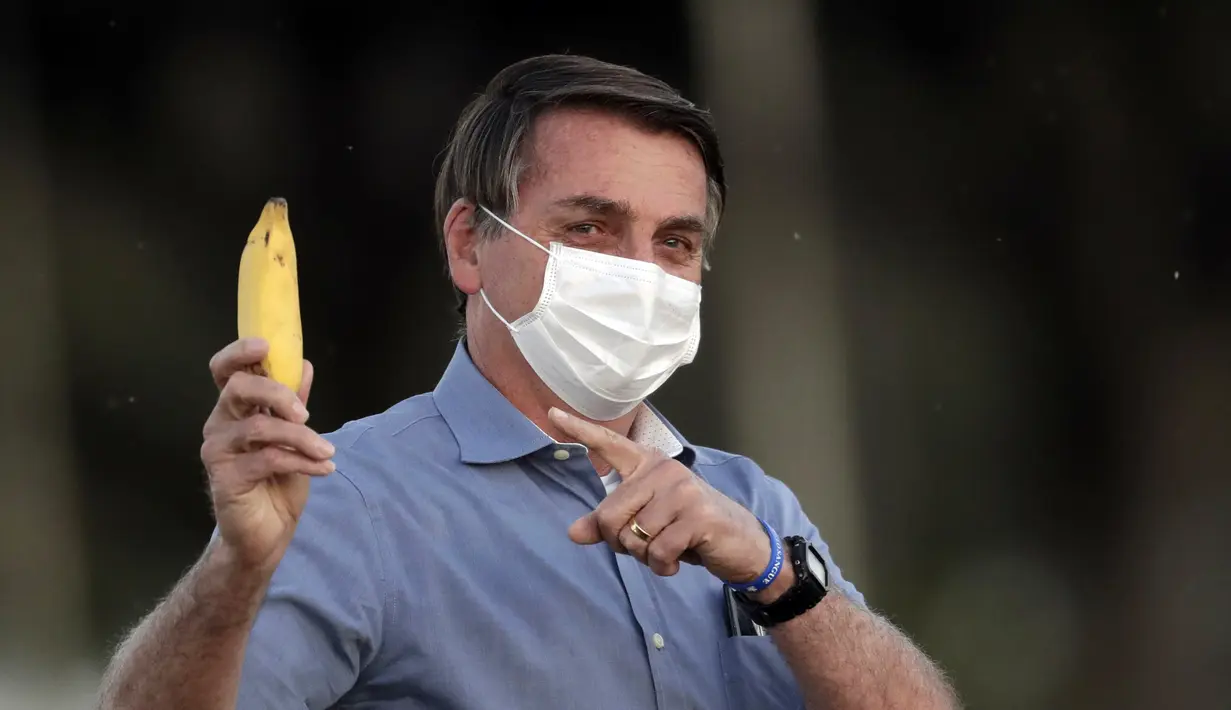Presiden Brasil Jair Bolsonaro mengenakan masker dan menunjukkan pisang kepada pers saat berbicara dengan para pendukungnya di luar Istana Alvorada, Brasilia, Brasil, Jumat (24/7/2020). Jair Bolsonaro dinyatakan positif terinfeksi COVID-19 pada 7 Juli lalu. (AP Photo/Eraldo Peres)