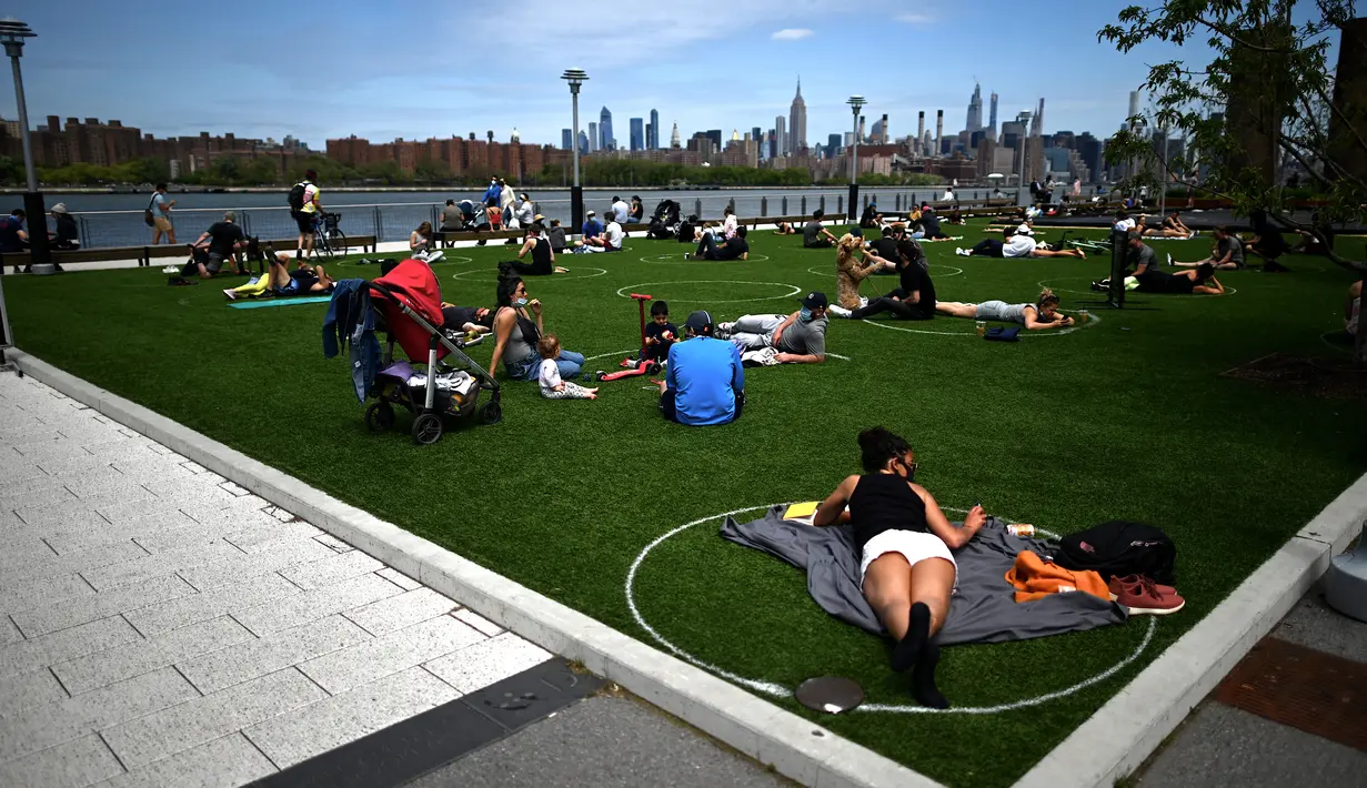 Orang-orang berusaha menjaga jarak dalam lingkaran putih saat bersantai di Domino Park, Brooklyn di Kota New York, Minggu (17/5/2020). Pengunjung taman berjemur dengan tetap menerapkan protokol penularan coorna Covid-19. (Photo by Johannes EISELE / AFP)