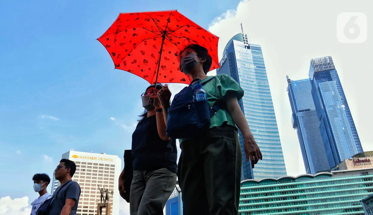 Warga menggunakan payung saat berjalan di tengah cuaca terik di kawasan Bundaran HI, Jakarta, Senin (24/4/2023). Badan Meteorologi Klimatologi dan Geofisika (BMKG) menyampaikan dinamika atmosfer yang tidak biasa menjadi salah satu penyebab Indonesia mengalami suhu panas dalam bebrapa hari terakhir. (Liputan6.com/Angga Yuniar)