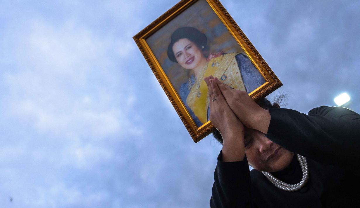 Seorang pelayat memegang potret Ratu Sirikit setelah iring-iringan mobil di Bangkok, Thailand pada Minggu 26 Oktober 2025. Persemayaman Ratu Sirikit berlangsung selama setahun dimulai pada 26 Oktober 2025 di Grand Palace, Bangkok, Thailand, setelah beliau meninggal dunia pada 24 Oktober 2025. (Chanakarn Laosarakham/AFP)