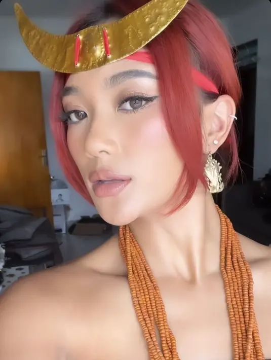 Marion Jola mengenakan aksesori kalung layering warna orange dengan ikat kepala model tanduk. Dengan rambut merahnya yang diikat. Serta anting-anting keemasannya. [@lalamarionmj]