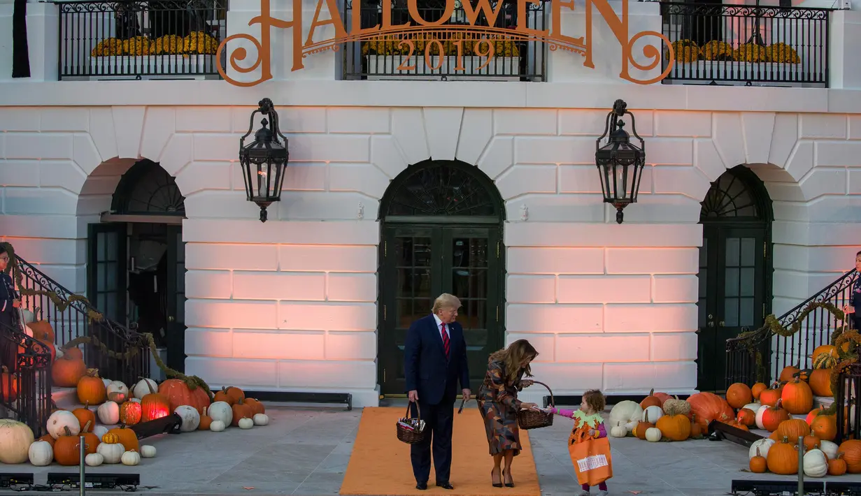 Presiden AS, Donald Trump dan ibu negara Melania Trump membagikan permen kepada anak-anak selama acara trick-or-treat Halloween di South Lawn, Gedung Putih, Senin (28/10/2019). Dalam acara ini anak-anak mengenakan kostum Halloween, sedangkan Donald dan Melania tetap tampil formal. (AP/Alex Brandon)