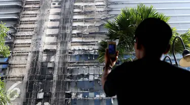 Seorang penghuni apartemen mengambil gambar Gedung Neo Soho pasca kebakaran di Tanjung Duren, Jakarta, Kamis (10/11). Kebakaran Gedung yang masih dalam tahap pembangunan itu terjadi Rabu (9/11) sekitar pukul 20.30. (Liputan6.com/Gempur M. Surya)