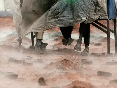 Pekerja migran India menutupi diri mereka dengan selembar plastik selama hujan di tempat pembakaran batu bata di pinggiran Kathmandu. Ribuan pekerja migran India datang ke Nepal untuk bekerja di pabrik batu bata. (AP Photo/Niranjan Shrestha)