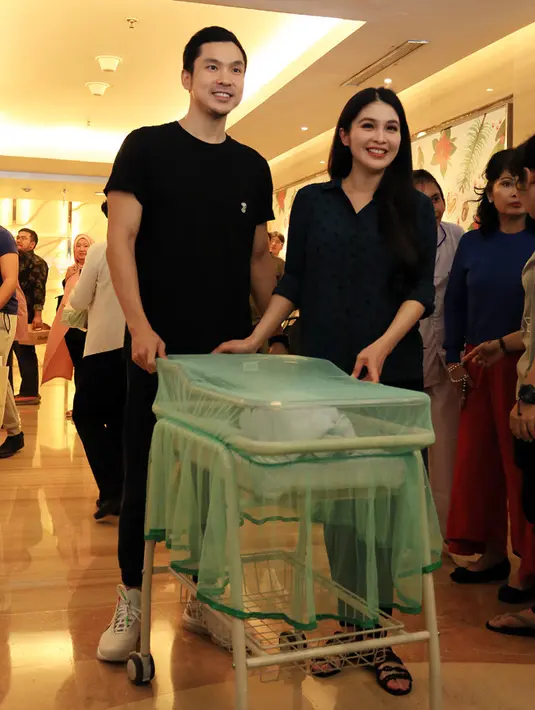Potret keceriaan ibu dan ayah baru Sandra Dewi saat meninggalkan Rumah Sakit Pondok Indah, Jakarta Selatan, Jumat (5/1/2018). Keduanya mendorong grobak bayi. (Deki Prayoga/Bintang.com)