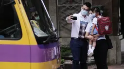 Seorang anak berfoto dengan orang tuanya sebelum menaiki bus sekolah di Hung Hom, Hong Kong, China selatan, pada 29 September 2020. Aturan menjaga jarak sosial (social distancing) sebagian telah dilonggarkan dan kehidupan masyarakat mulai kembali normal. (Xinhua/Wang Shen)