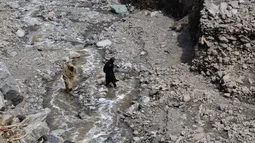 Seorang wanita menyebrangi sungai setelah jalanan rusak akibat banjir bandang di Ursoon, daerah terpencil Chitral di Pakistan utara, Minggu (3/7). Banjir merusak sejumlah rumah dan sebuah masjid dengan jumlah korban tewas 43 orang (GUL HAMAAD Farooqi/AFP)