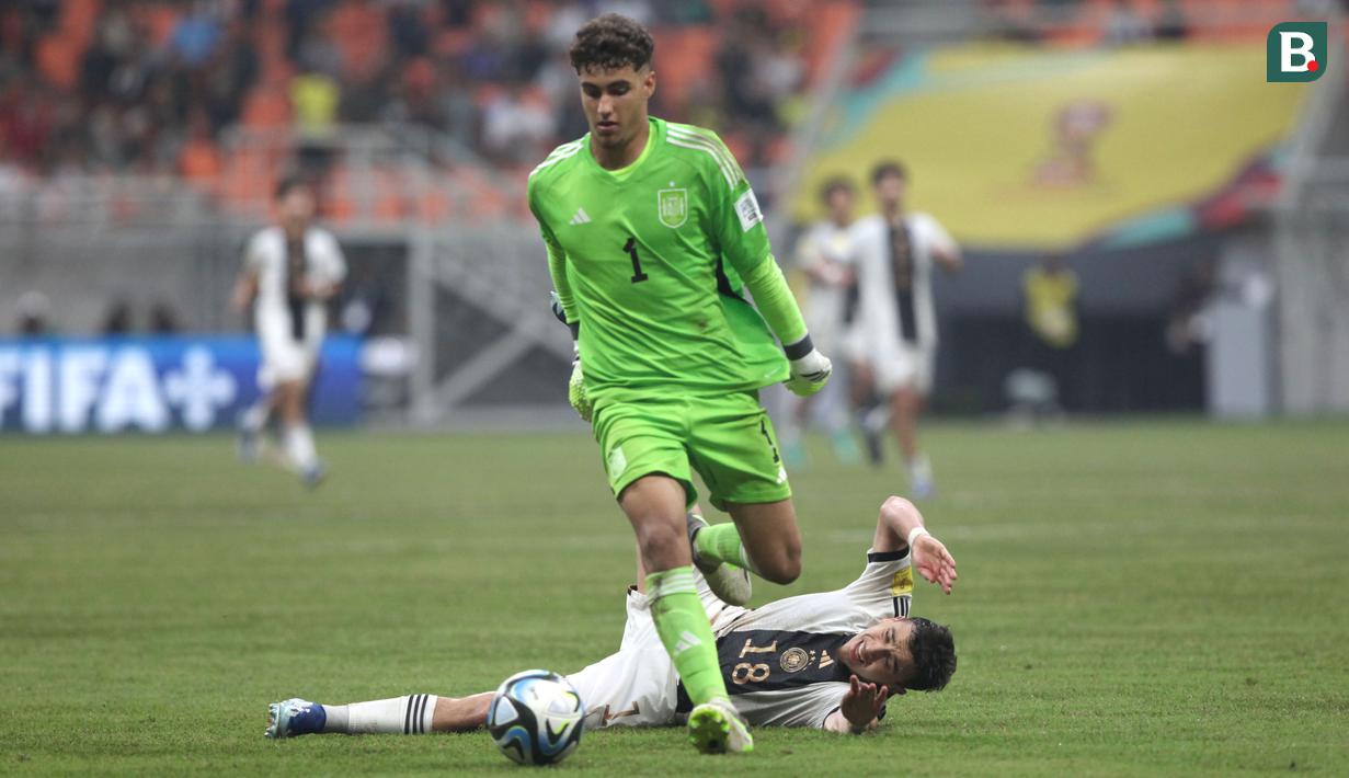 Pemain Timnas Jerman U-17, Bilal Yalcinkaya (kanan), terjatuh setelah mendapatkan gangguan dari kiper Timnas Spanyol U-17, Raul Jimenez, saat pertandingan perempat final Piala Dunia U-17 2023 yang berlangsung di Jakarta International Stadium, Jumat (24/11/2023). (Bola.com/Arief Bagus)