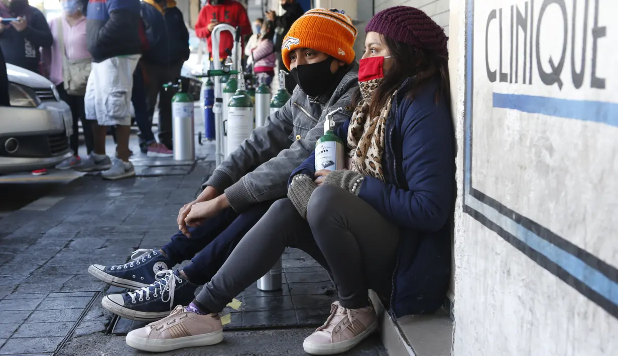 Jonatan Camacho dan istrinya Areli Bravo menunggu di trotoar untuk mengisi dua tangki oksigen di Mexico City pada 27 Desember 2020. Lonjakan pasien terinfeksi virus corona yang dirawat di Mexico City membuat toko pasokan medis kekurangan pasokan isi ulang tabung oksigen. (AP Photo/Ginnette Riquelme)