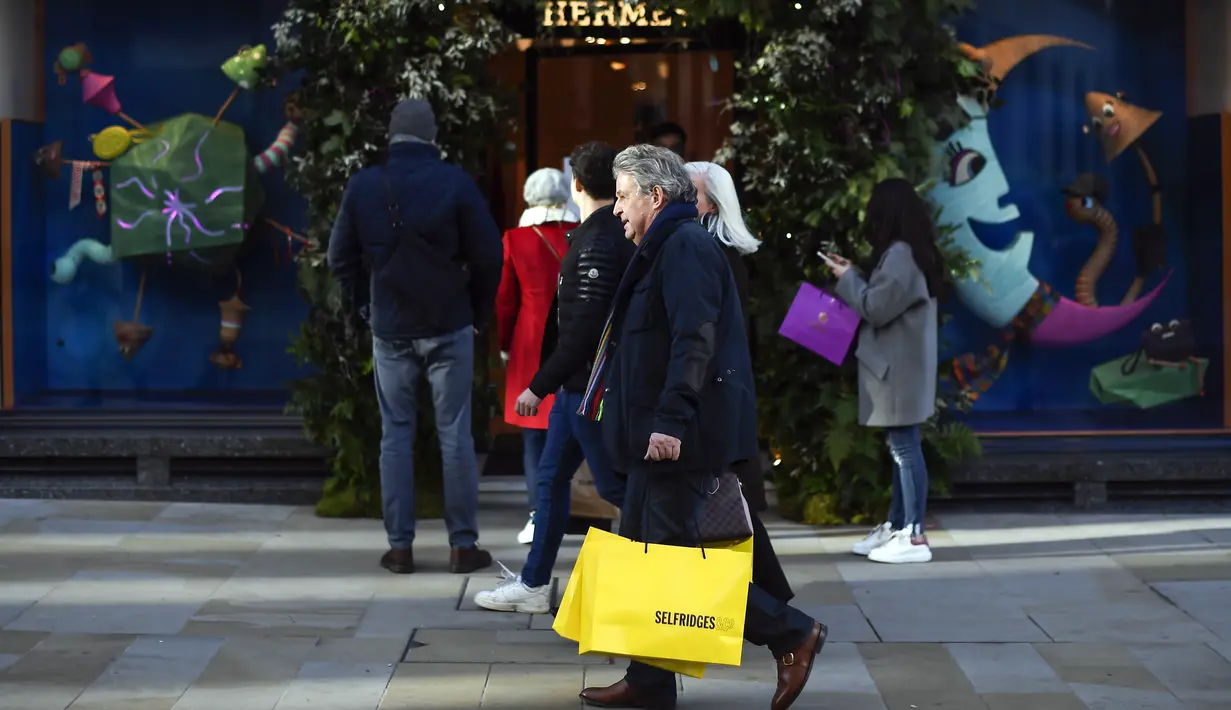 Orang-orang berjalan melewati toko sambil membawa tas belanja di Mayfair setelah pelonggaran pembatasan virus corona COVID-19 menyusul berakhirnya kebijakan penguncian nasional atau lockdown kedua di Inggris, di London, Sabtu (5/12/2020). (AP Photo/Alberto Pezzali)
