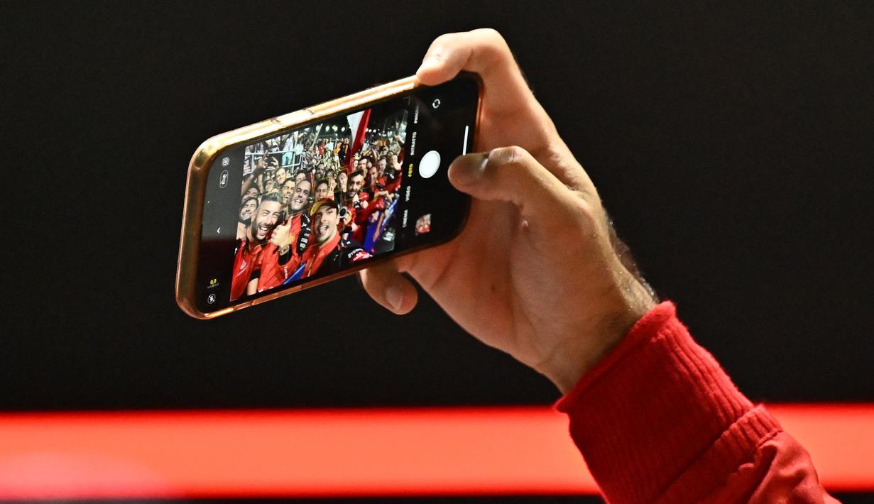 Pembalap tim Scuderia Ferrari, Carlos Sainz melakukan selfie dengan timnya saat perayaan kemenangan balapan F1 GP Singapura 2023 di Marina Bay Street Circuit, Singapura, Minggu (17/9/2023) malam WIB. (AFP/Lillian Suwanrumpha)