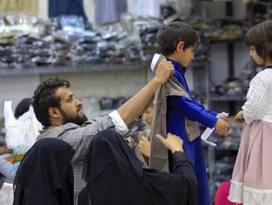 Warga Yaman membantu memilihkan pakaian baru untuk anak-anak mereka di ruang pamer yang membagikan pakaian kepada para pemuda yang kehilangan orang tua dalam konflik, sebagai bagian dari kegiatan amal selama bulan suci Ramadhan, di ibu kota Sanaa (8/4/2022). (AFP/Mohammed Huwais)