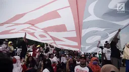 Massa berteduh di bawah bendera raksasa bertuliskan '#2019GantiPresiden' saat deklarasi akbar di Monas, Jakarta, Minggu (6/5). Acara ini juga diramaikan dengan penjualan kaus dan atribut bertagline #2019GantiPresiden. (Merdeka.com/Iqbal Nugroho)