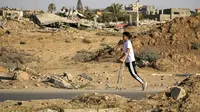 Seorang anak Palestina yang kakinya diamputasi berjalan di sepanjang jalan, melewati bangunan-bangunan yang hancur selama pemboman Israel, di kamp pengungsi al-Bureij di Jalur Gaza tengah pada 24 Juni 2024. (Eyad BABA/AFP)