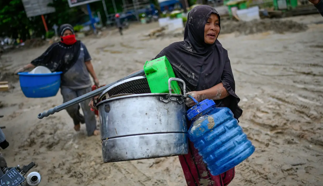 Penduduk desa membawa barang-barang dari rumah mereka sebelum mengungsi setelah banjir bandang di Kabupaten Luwu Utara, Sulawesi Selatan, Rabu (15/7/2020).  Akibat banjir bandang tersebut mengakibatkan 16 orang meninggal dunia dan ratusan rumah tertimbun lumpur. (Hariandi HAFID / AFP)