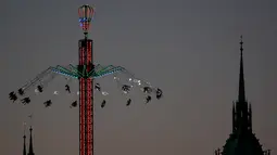 Pengunjung menaiki wahana ayunan ontang-anting di depan gereja St. Paul saat festival bir Oktoberfest di Munich, 27 September 2018. Festival yang merupakan salah satu acara paling terkenal di Jerman ini sudah ada sejak tahun 1800an. (AP/Matthias Schrader)