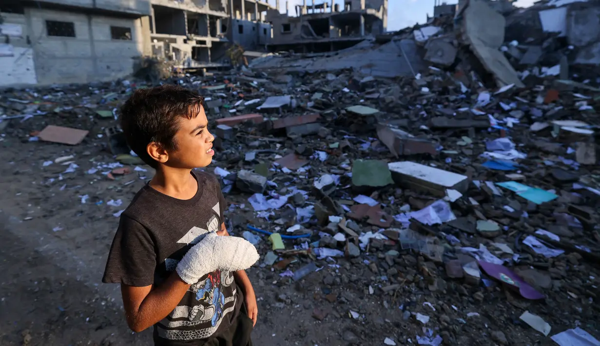 Seorang anak laki-laki Palestina yang terluka, Mohammed Sofi, 12 tahun, melihat bangunan yang hancur akibat serangan udara Israel di dekat rumahnya di kamp pengungsi Rafah, selatan Jalur Gaza, pada 16 Oktober 2023. (MOHAMMED ABED/AFP)