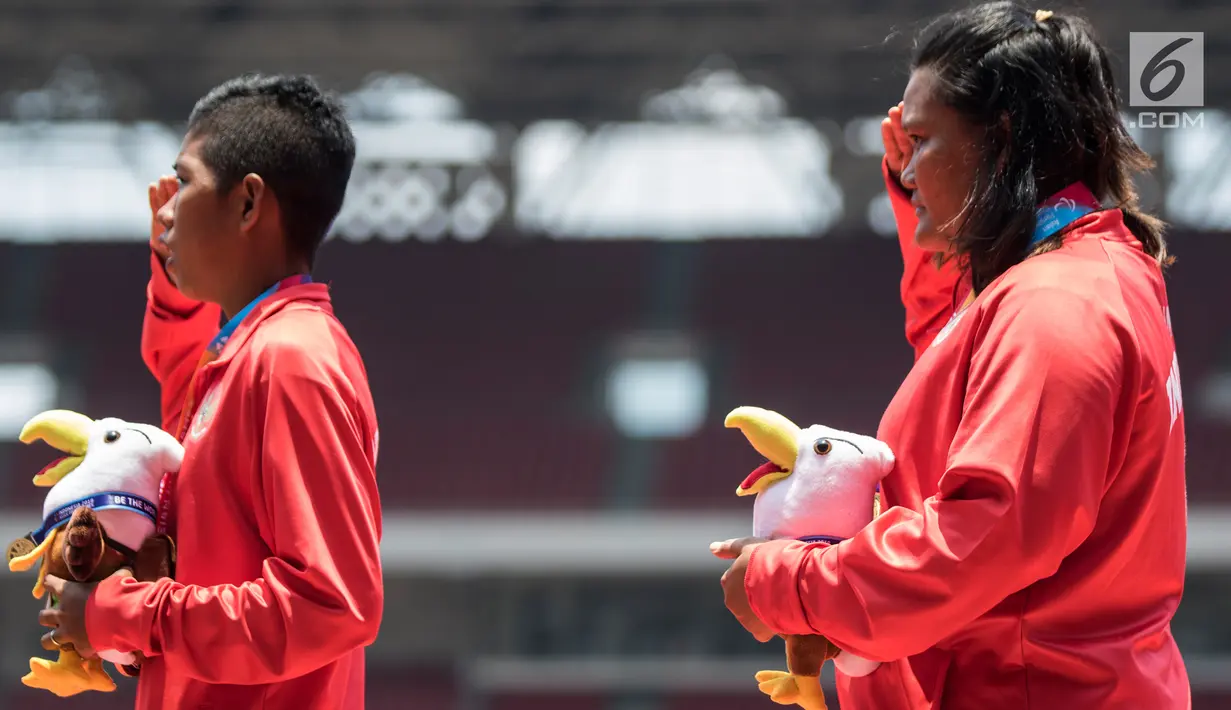 Atlet tolak peluru Indonesia, Suparniyati (kanan) hormat bendera saat seremoni usai meraih medali emas Asian Para Games 2018 di SUGBK, Jakarta, Senin (8/10). Suparniyati mencatat tolakan sejauh10,75 meter. (Bola.com/Vitalis Yogi Trisna)