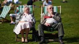 Sepasang lansia bersantai menikmati sinar matahari di atas kursi di Green Park, pusat kota London, Rabu (4/5). Awal Mei, suhu udara hangat mulai menyelimuti kota London. (Niklas HALLE'N/AFP)