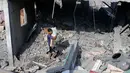 Seorang bocah tampak mencari sisa barang kepunyaan miliknya di antara reruntuhan bangunan akibat serangan udara Israel (REUTERS/Ibraheem Abu Mustafa)