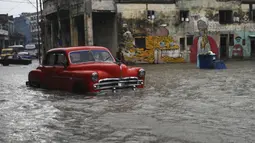 Sebuah mobil tua Amerika Serikat melewati jalan yang banjir di Havana, Kuba, 30 Juni 2021. Hujan deras dan selokan yang tidak berfungsi menyebabkan banjir di jalan-jalan di Havana. (YAMIL LAGE/AFP)