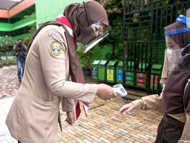 Guru memeriksa suhu tubuh siswa saat hari pertama uji coba Pembelajaran Tatap Muka (PTM) di SDN Kenari 08 Pagi, Jakarta, Rabu (7/4/2021). Pemprov DKI Jakarta mulai melakukan uji coba pembelajaran tatap muka secara terbatas di 100 sekolah mulai 7 hingga 29 April 2021. (Liputan6.com/Faizal Fanani)
