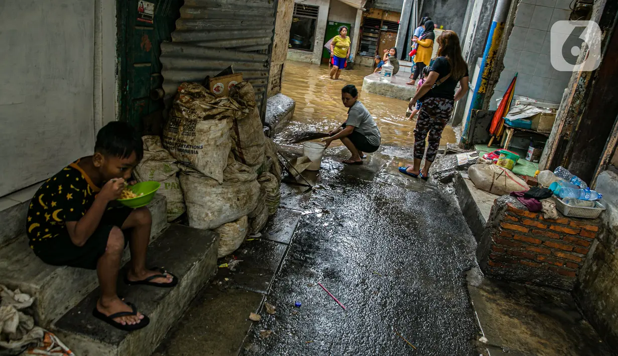 Seorang anak makan saat sejumlah warga bersih-bersih usai banjir di permukiman kawasan Kampung Melayu, Jakarta, Selasa (9/2/2021). Banjir yang berangsur surut dimanfaatkan warga untuk membersihkan rumah dan barang-barang dari endapan lumpur. (Liputan6.com/Faizal Fanani)