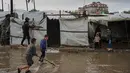 Air terlihat menggenangi jalanan dan memasuki tenda. Tampak dalam foto, anak-anak pengungsi Palestina berjalan melewati kamp tenda yang basah kuyup akibat hujan lebat di Deir al-Balah, Jalur Gaza tengah, Kamis, 26 Maret 2026. (AP Photo/Abdel Kareem Hana)