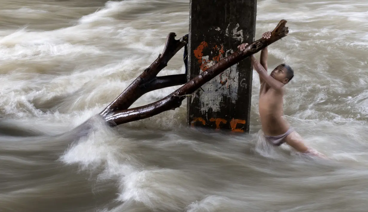 Seorang bocah laki-laki memegang batang pohon saat ia bermain di sungai dengan arus yang sangat deras akibat hujan lebat di bawah jembatan di Manila, Filipina (11/6). (AFP Photo/Noel Celis)