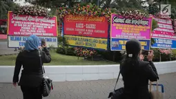 Sejumlah orang menggunakan ponselnya mengambil gambar karangan bunga ucapan selamat atas pelantikan Gubernur dan Wakil Gubernur DKI terpilih, Anies Baswedan dan Sandiaga Uno di Halaman Balai Kota DKI Jakarta, Senin (16/10). (Liputan6.com/Faizal Fanani)