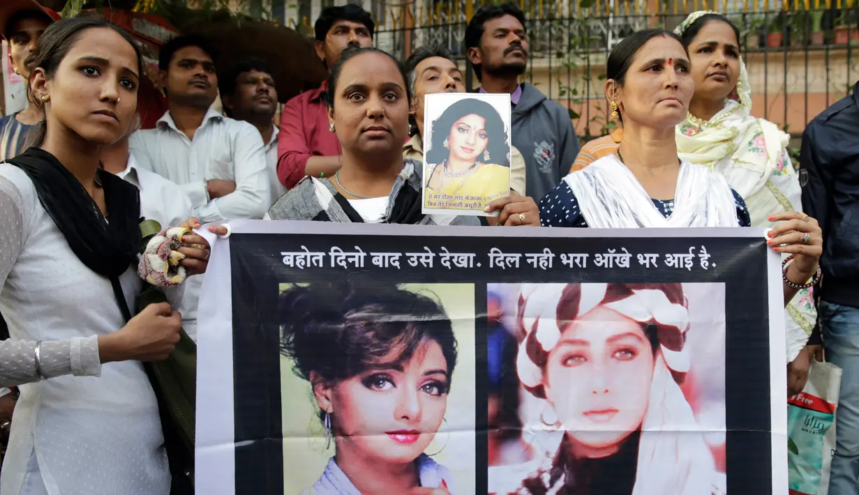 Fans aktris Bollywood Sridevi Kapoor memegang poster sang mendiang saat berdiri di luar rumah jelang pemakamannya, Mumbai, India, Rabu (28/2). (AP Photo/Rafiq Maqbool)
